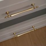 "Brass pull bar handles with a tapered spindle design and intricate finials on light grey drawers."