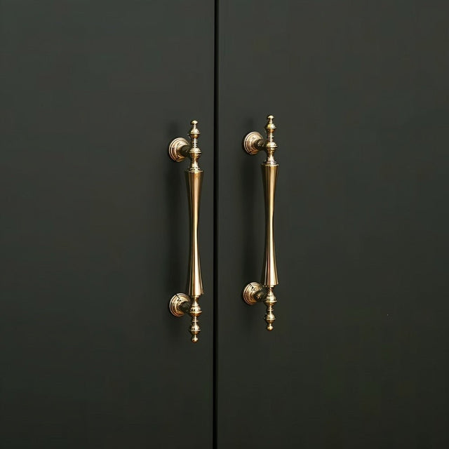 "Pair of brass handles with a tapered spindle design and intricate finials on a dark-colored cabinet."