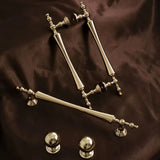 "Set of brass knobs and pull bar handles with a tapered spindle design and intricate finials on a dark brown surface."