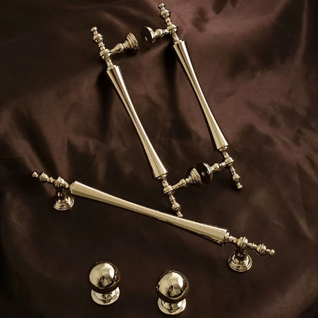 "Set of brass knobs and pull bar handles with a tapered spindle design and intricate finials on a dark brown surface."