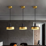 "Three pendant lights with black marble and brass detailing hang from a ceiling, providing warm, focused illumination."