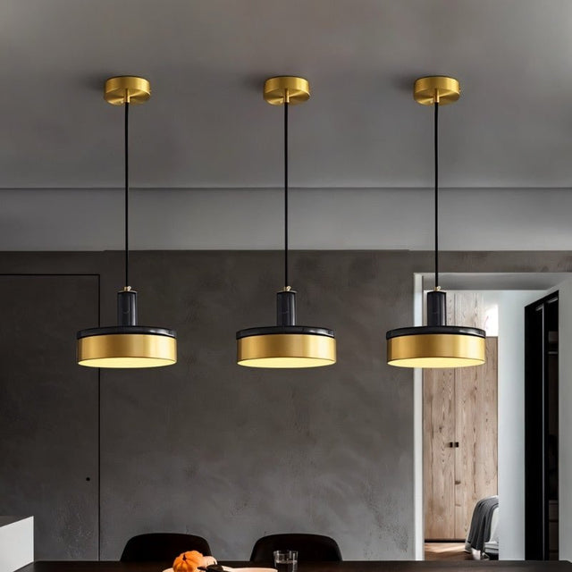 "Three pendant lights with black marble and brass detailing hang from a ceiling, providing warm, focused illumination."