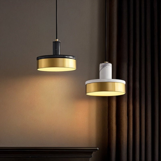 "Two modern pendant lights, one with black marble and the other with white marble and brass accents, hang in a dimly lit room."