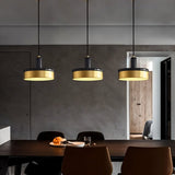 "Three pendant lights with black marble and brass accents hang above a modern dining table, casting a warm and inviting glow."