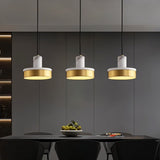 "Three pendant lights with white marble and brass accents hang over a modern kitchen island, illuminating the space with a warm glow."