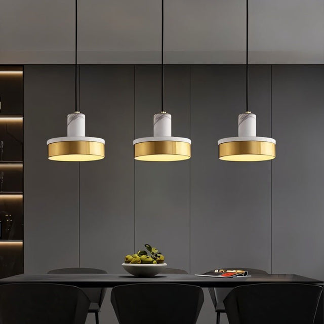 "Three pendant lights with white marble and brass accents hang over a modern kitchen island, illuminating the space with a warm glow."