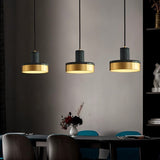"Three modern pendant lights with black marble and brass accents hang over a dining table, creating a warm and stylish ambiance."