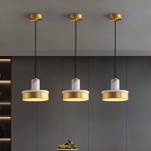 "Three pendant lights with white marble and brass accents hang in a modern space, providing a soft, ambient glow."