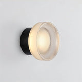 "A modern, minimalist wall lamp with a circular glass diffuser and a sleek black frame, emitting a soft, ambient glow."