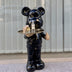 Black bear figurine with clock face and holding a serving tray with cosmetic products, giving a thumbs up gesture.