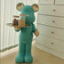 Turquoise bear figurine with wooden ears holding a tray of nuts, standing on a wooden floor beside white furniture.