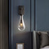 Pulcher Glass Tears wall sconce with clear glass and black metal mounting, mounted on a dark blue wall in a modern bedroom.