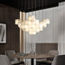 Alabaster cube pendant chandelier with warm lighting suspended above a round dining table with gray chairs.
