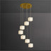 Multi-pendant chandelier with seven stacked alabaster cube shades and brass ceiling canopy against a gray wall.