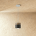 Three cylindrical pendant lights with white shades and natural wood tops hanging at different heights against a white wall.