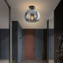 Smoked glass ceiling light with black metal finish illuminating a modern hallway with gray and terracotta walls.