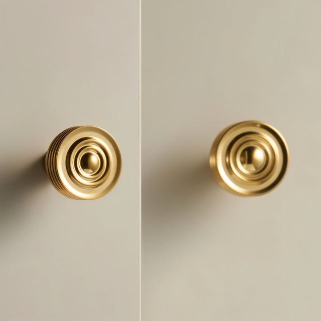 "Pair of brass knobs with concentric ring design and ridged surface mounted on a light gray cabinet."