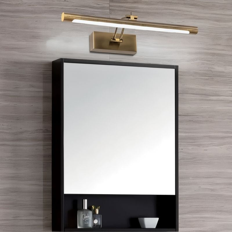 "A gold wall lamp with a linear LED bar illuminating a dark medicine cabinet with a mirror and small bottom shelf, mounted on a textured wall."