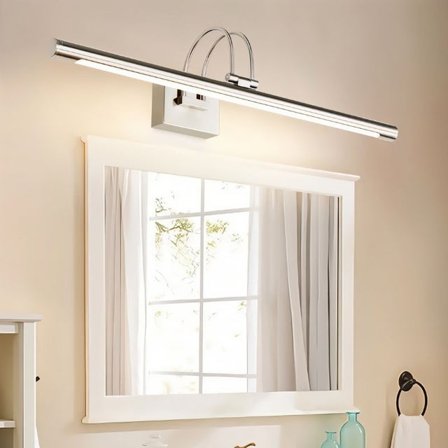 "A silver wall lamp with a linear LED bar illuminating a white framed bathroom mirror, reflecting a window with natural light."