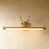 Brass deer head vanity light above round gold-framed mirror against gray wall in studio setting