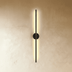 Black vertical linear wall sconce with warm glow on white wall in modern residential interior with dark wood cabinetry.