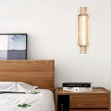 "Modern crystal wall lamp with a vertical, cylindrical design, mounted on a wall in a contemporary bedroom."