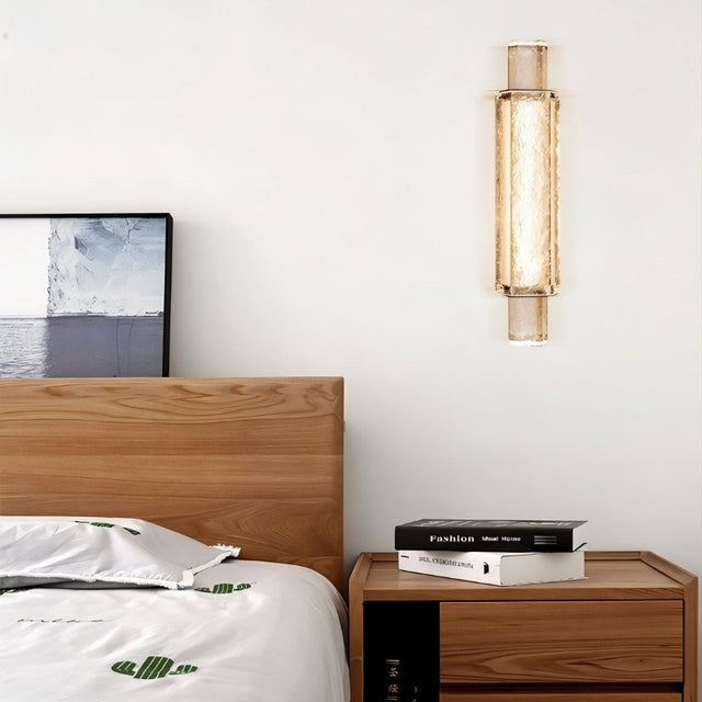 "Modern crystal wall lamp with a vertical, cylindrical design, mounted on a wall in a contemporary bedroom."