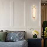 "Modern crystal wall lamp with a vertical, cylindrical design, providing soft lighting in a contemporary bedroom."