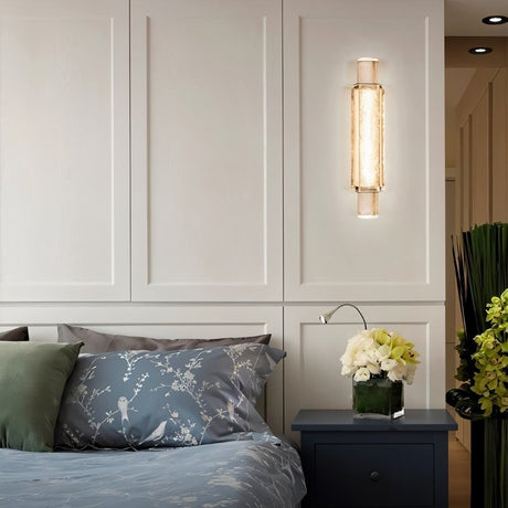"Modern crystal wall lamp with a vertical, cylindrical design, providing soft lighting in a contemporary bedroom."
