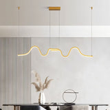 "A gold wave-like pendant light with a sculptural design, suspended above a dining table, providing diffused and elegant illumination."