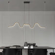 "A wave-like pendant light with a sculptural design, suspended above a modern dining table, providing diffused illumination."