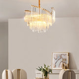 "A tiered chandelier with clear crystal rods and a brass frame, hanging above a dining table in a well-lit room with artwork."