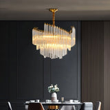 "A tiered chandelier with clear crystal rods and a brass frame, illuminating a dining room with a dark accent wall."