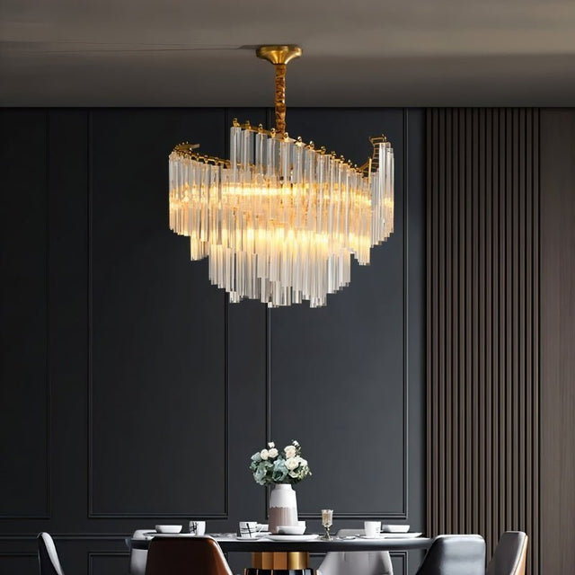 "A tiered chandelier with clear crystal rods and a brass frame, illuminating a dining room with a dark accent wall."