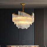 "A tiered chandelier with clear crystal rods and a brass frame, hanging in a modern living room with dark walls."