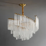 "A tiered chandelier with clear crystal rods and a brass frame, suspended against a plain grey backdrop."