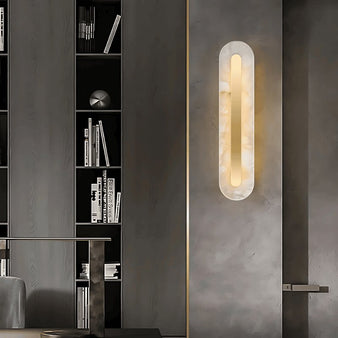 "Contemporary alabaster and brass wall lamp with soft glow, mounted in a modern interior with dark shelving"