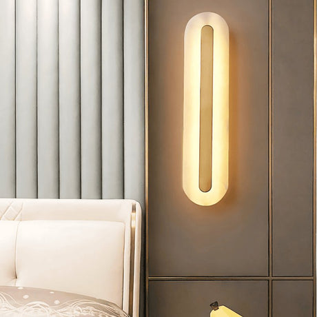 "Elegant alabaster and brass wall lamp emitting warm light, installed beside a bed in a luxurious bedroom setting"
