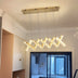Modern wave-shaped LED chandelier with brass finish and crystal accents suspended in a contemporary living room with white ceiling and large windows.
