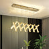 Modern gold LED chandelier with twisted geometric design suspended above a dining table with plants.
