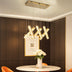 Modern brass X-shaped pendant chandelier with crystal panels hanging above a round marble table in an elegant dining room.