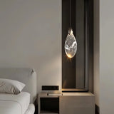 "A single, uniquely shaped crystal pendant light hangs next to a bed in a modern bedroom, casting a warm, ambient glow."