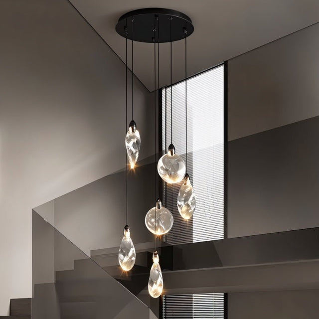 "A group of uniquely shaped crystal pendant lights hang from a round, black canopy in a modern stairwell, casting a warm light and creating a sculptural effect."