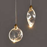 "Two uniquely shaped crystal pendant lights, one round and one oval, with gold caps, hang against a grey background, showcasing their elegant design and warm light."
