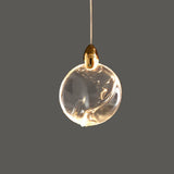 "A single, sphere-shaped crystal pendant light with a gold cap, emitting a warm glow against a grey background."
