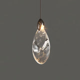 "A single, teardrop-shaped crystal pendant light with a dark metallic top, casting a warm glow against a grey background."