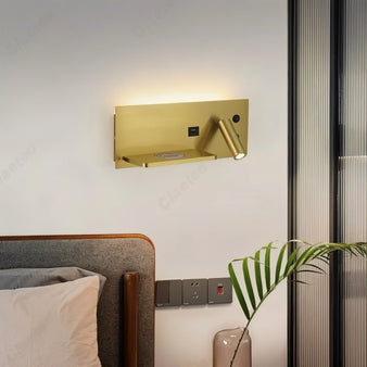 "Gold-finished wall-mounted bedside lamp with adjustable spotlight, USB port, and wireless charging pad, installed beside a bed in a modern bedroom."