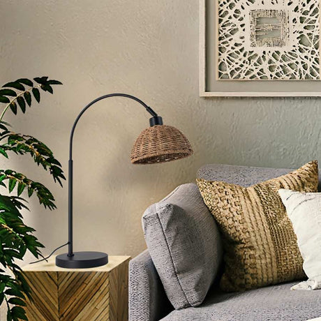 "A modern table lamp with a handwoven Lafite grass dome shade in a living room with a grey sofa and a framed picture."