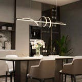 "A modern black linear pendant light with wave-like curves, hanging above a dining table in a modern dining room with a plant and decor."