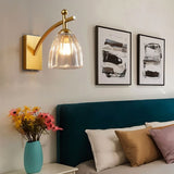 "A gold wall lamp with fluted glass shade in a bedroom setting."